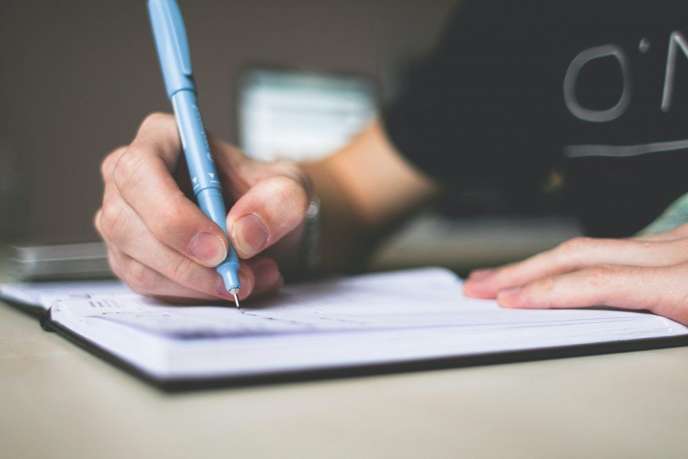 A person holding a blue ballpoint pen writing in a notebook